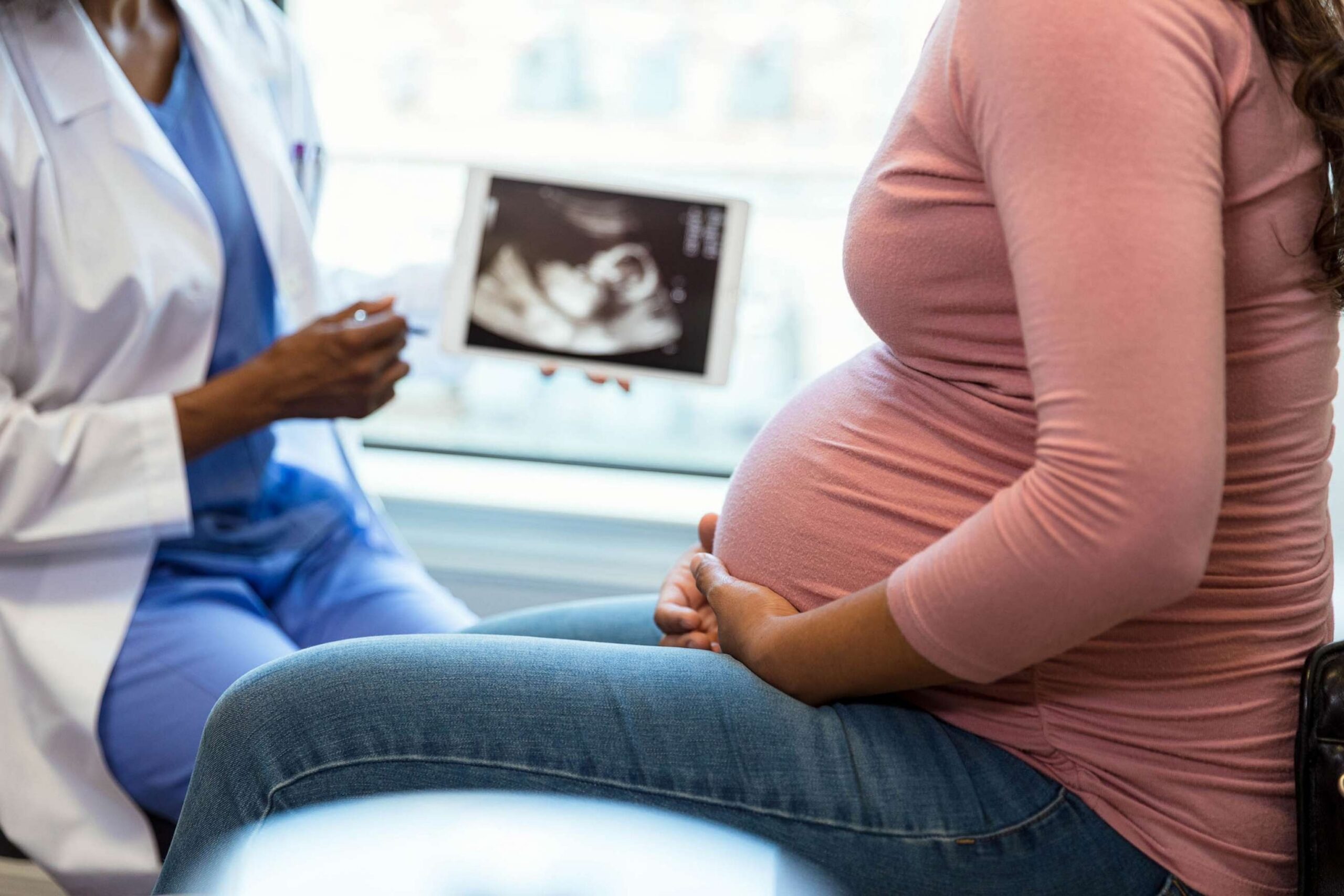 A clinician reviews an ultrasound image on a tablet with a seated expectant mother