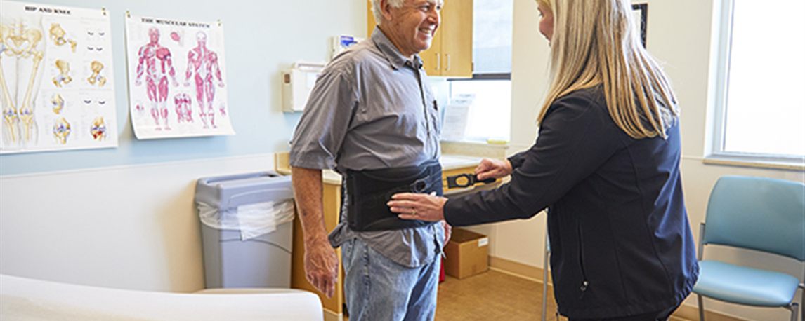 An Active Medical fitter adjusts a lumbar back brace on a standing patient in a fitting room