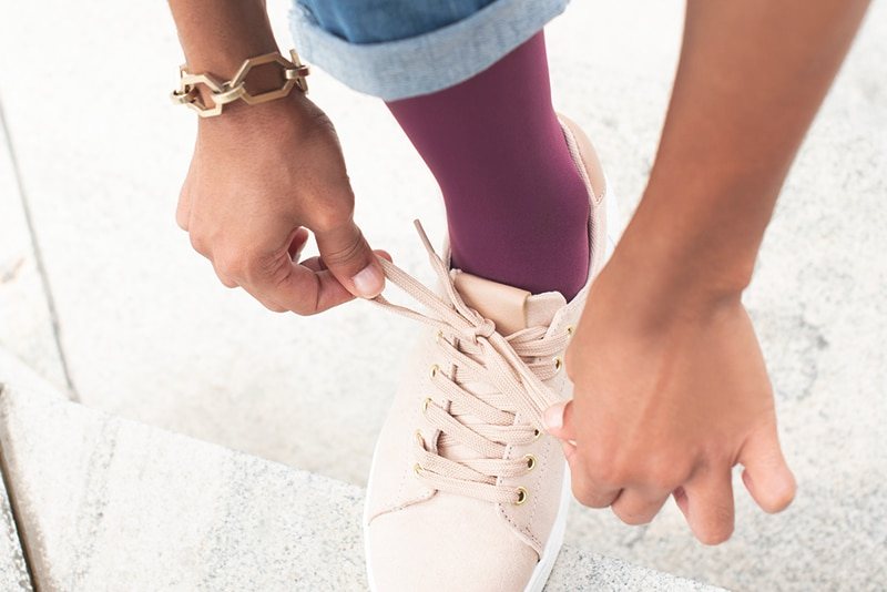 Person tying a sneaker while wearing a burgundy JOBST compression stocking