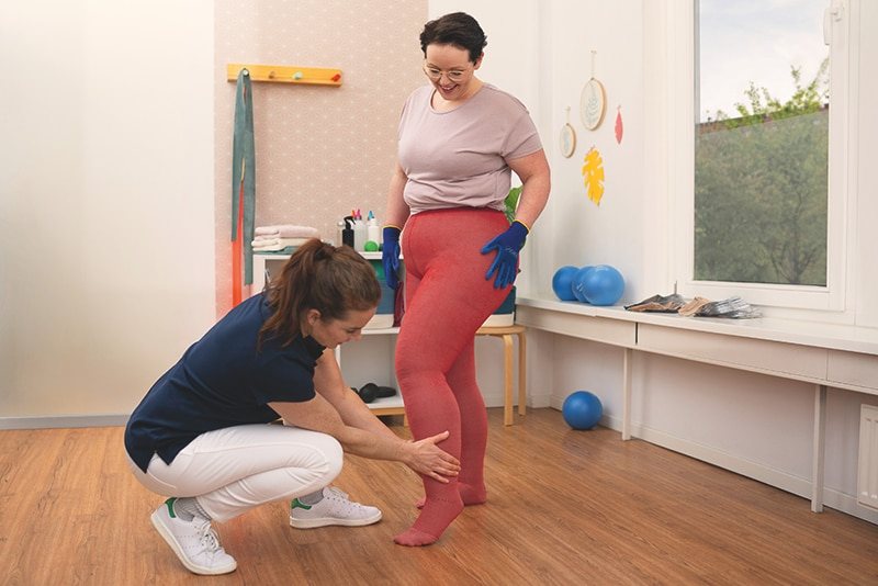 Fitter helping a patient put on a red JOBST compression stocking