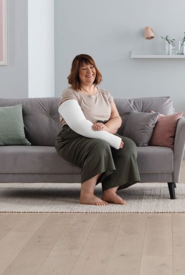 Woman relaxing on a sofa wearing a white Juzo compression arm sleeve