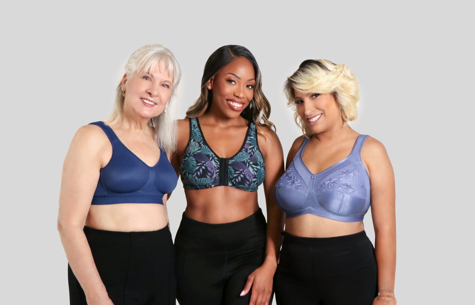 Three women wearing mastectomy bras in navy mesh, tropical print front-closure and lavender embroidered styles